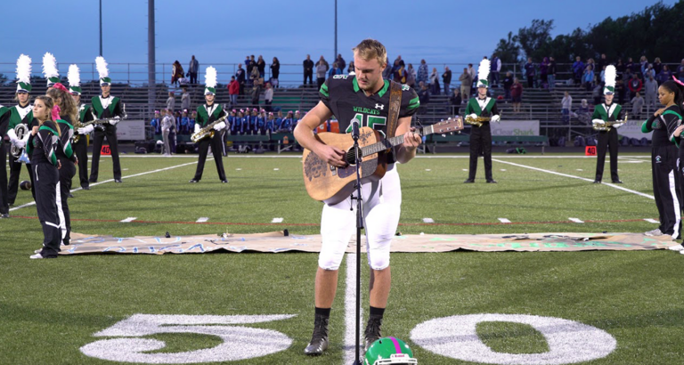 When no one volunteered to sing the national anthem, a high school student removed his helmet and picked up a guitar